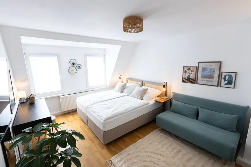 Doppelbett unter der Dachschräge, daneben ein petrolfarbenes Sofa und eine Zimmerpflanze