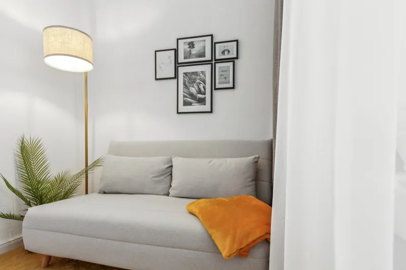 Helles Sofa mit orangefarbener Decke, Stehleuchte und Bilderwand
