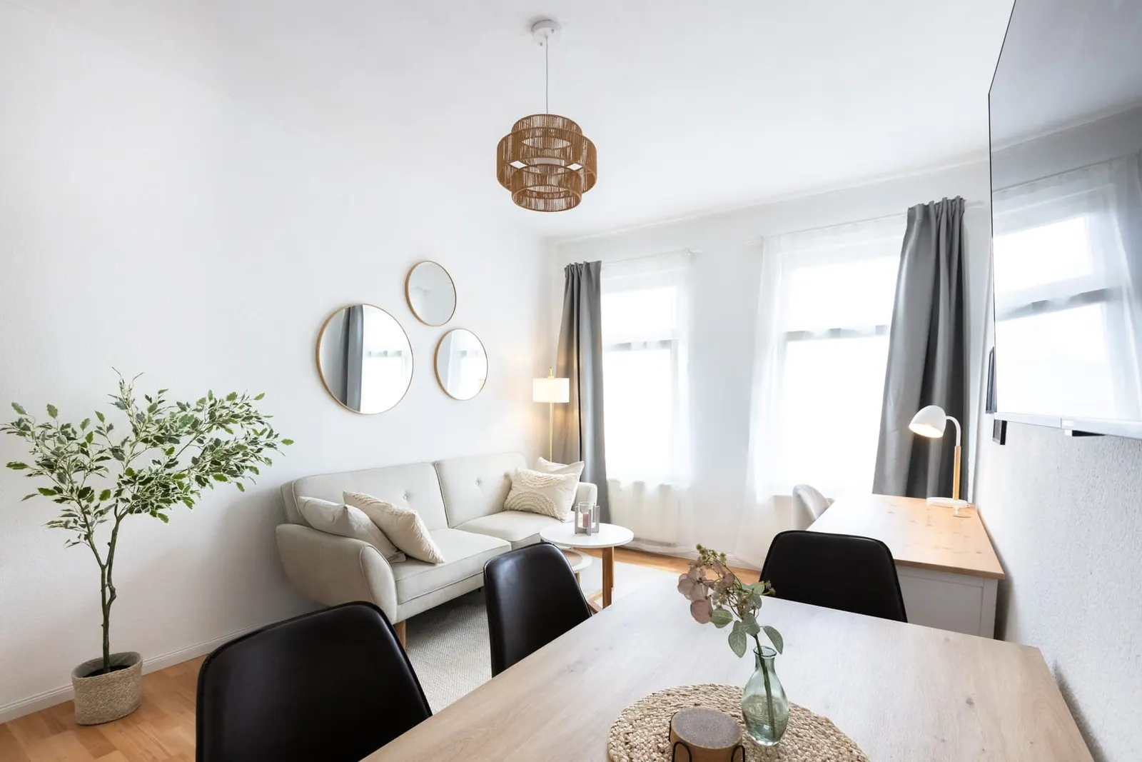 Wohnbereich mit hellem Sofa, runden Spiegeln und Esstisch vor hohen Fenstern