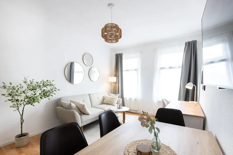 Wohnbereich mit hellem Sofa, runden Spiegeln und Esstisch vor hohen Fenstern