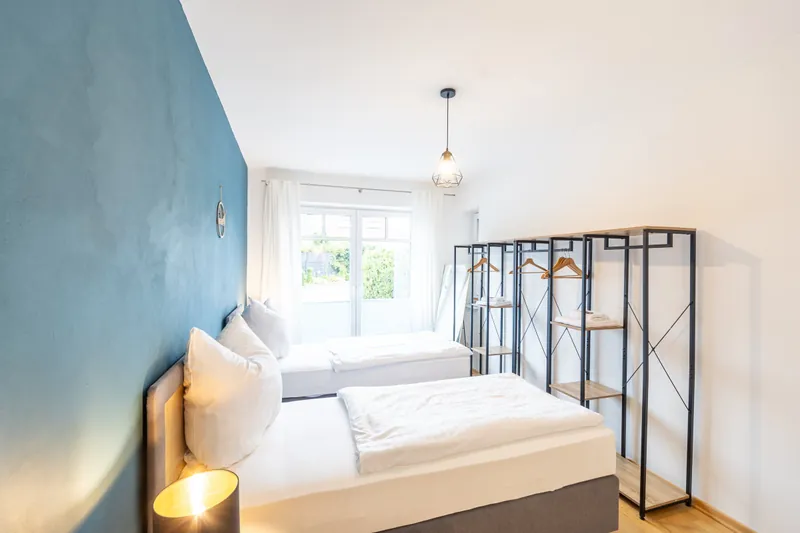 Schlafzimmer mit petrolfarbener Wand, frisch bezogenem Bett und Nachttischlampe