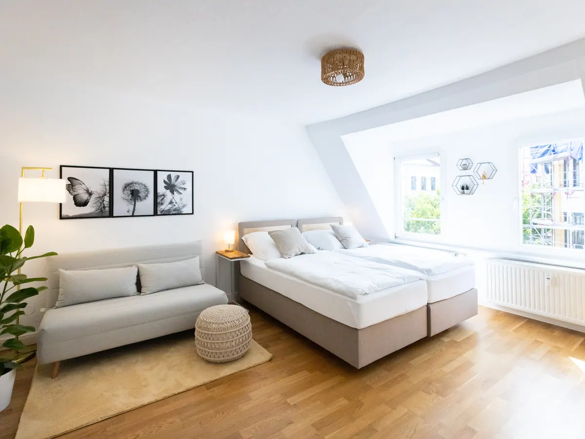 Helles Dachgeschosszimmer mit Doppelbett, Sofa, Zimmerpflanze und Gaubenfenster