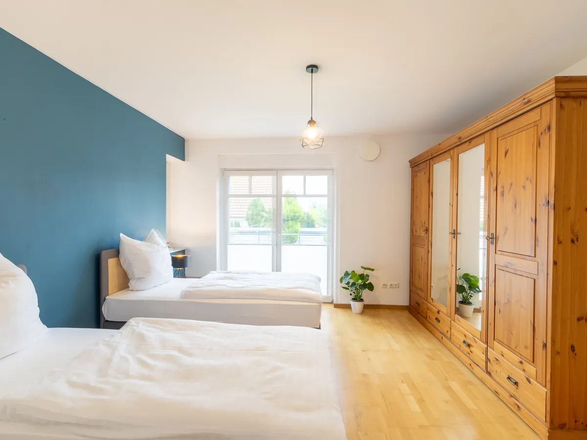 Schlafzimmer mit petrolfarbener Wand, zwei Betten, großem Holzschrank und Fenstertür