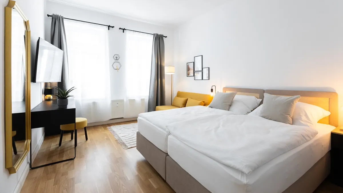 Schlafzimmer mit großem Doppelbett, gelbem Schlafsofa, warm leuchtenden Lampen und Goldspiegel